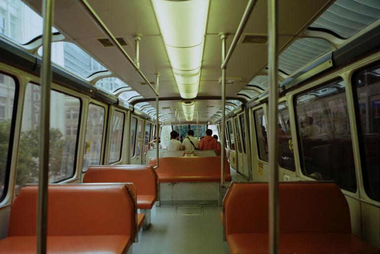The interior of a monorail car with orange seats and a few passengers in the distance.