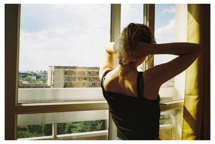 A woman with her back to the viewer stretches while looking out a window at an urban landscape.