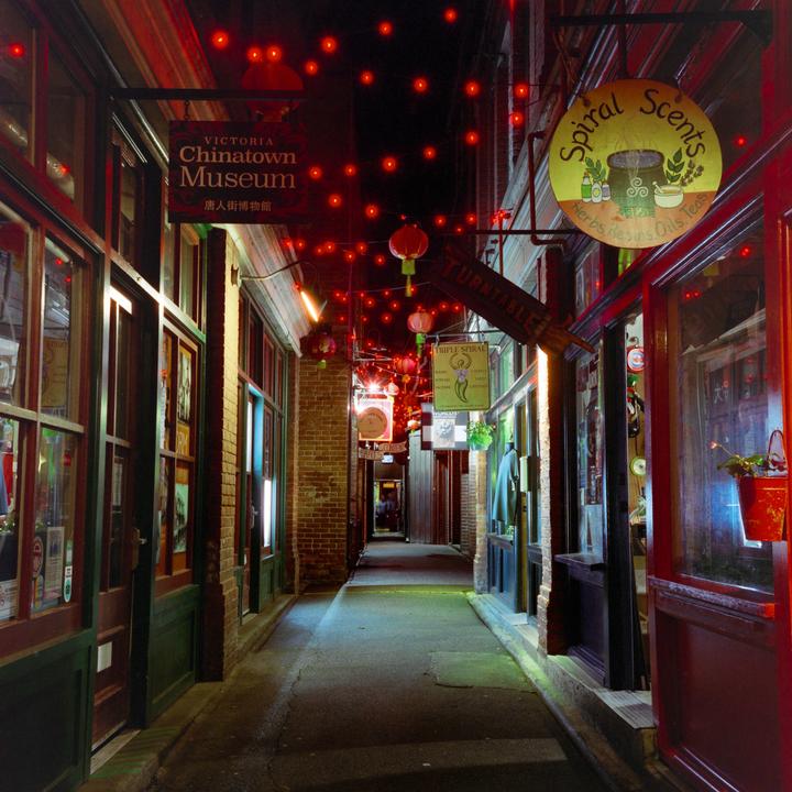 A narrow alleyway is illuminated by red string lights and lanterns, with storefronts and signs visible on both sides.
