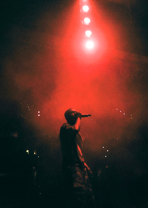 A man performs on stage under a bright red spotlight.