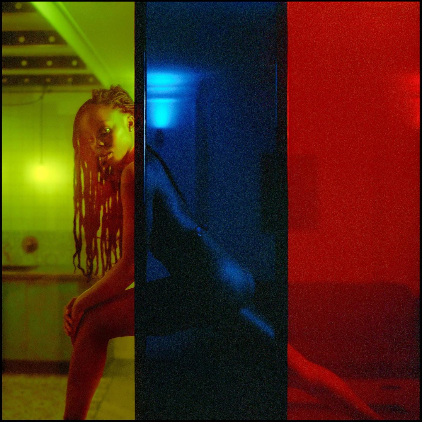 A woman with dreadlocks sits in a room with green, blue, and red lighting.
