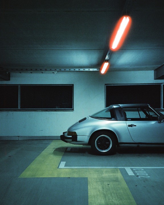 A silver car is parked in a garage under red neon lights.