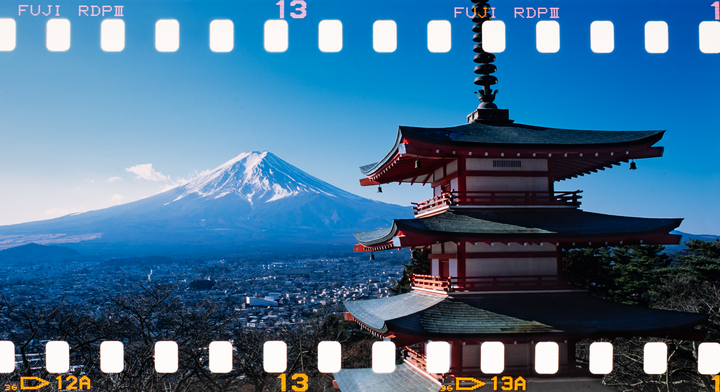 A red pagoda stands in the foreground with Mount Fuji in the background, overlooking a town.