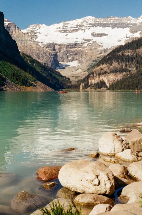 A turquoise lake is surrounded by mountains with snow-capped peaks and evergreen forests.
