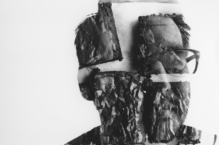 A man with glasses is visible through a double exposure with tree bark.