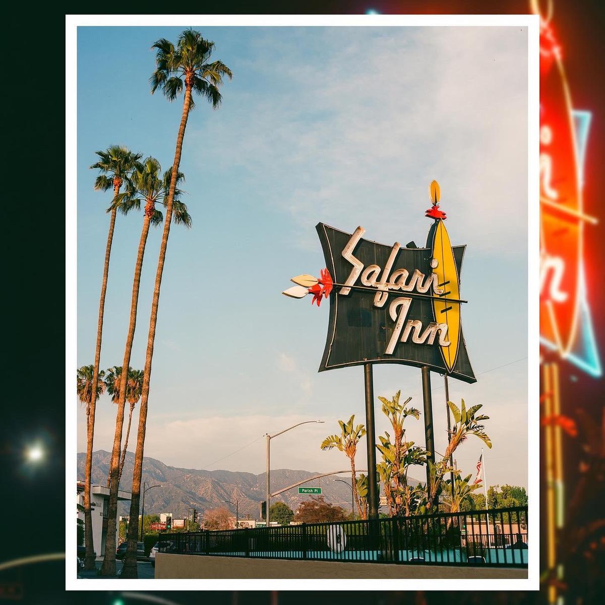 A sign for Safari Inn stands tall against a clear sky, flanked by palm trees and distant mountains.