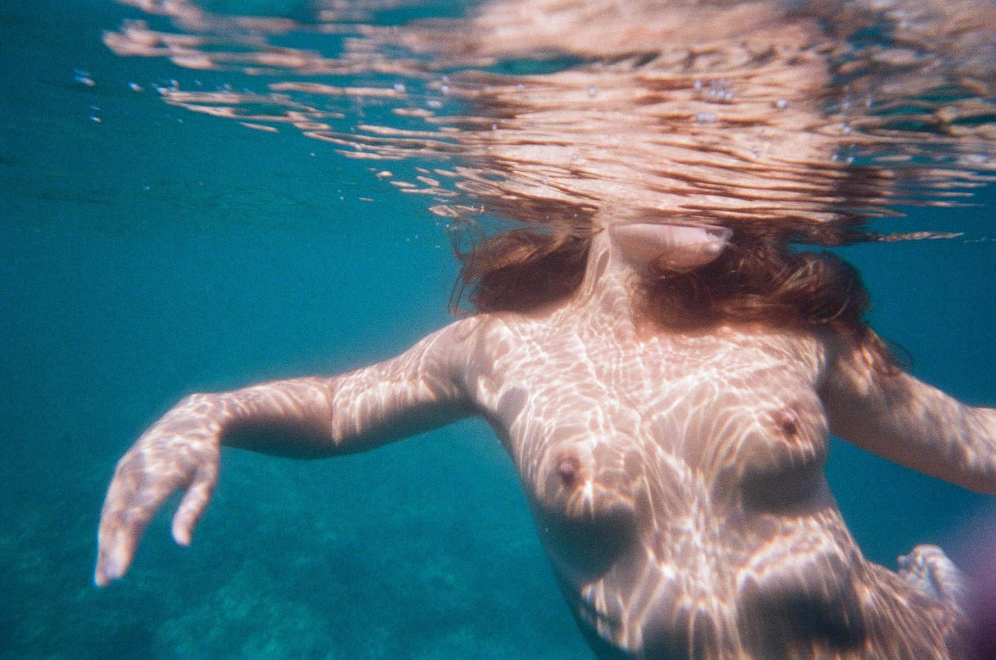 A woman swims underwater with light patterns reflecting on her body.