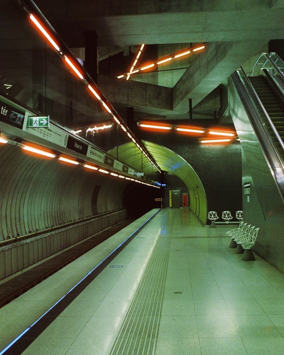 An empty subway platform with orange lights and an escalator leading up is visible.
