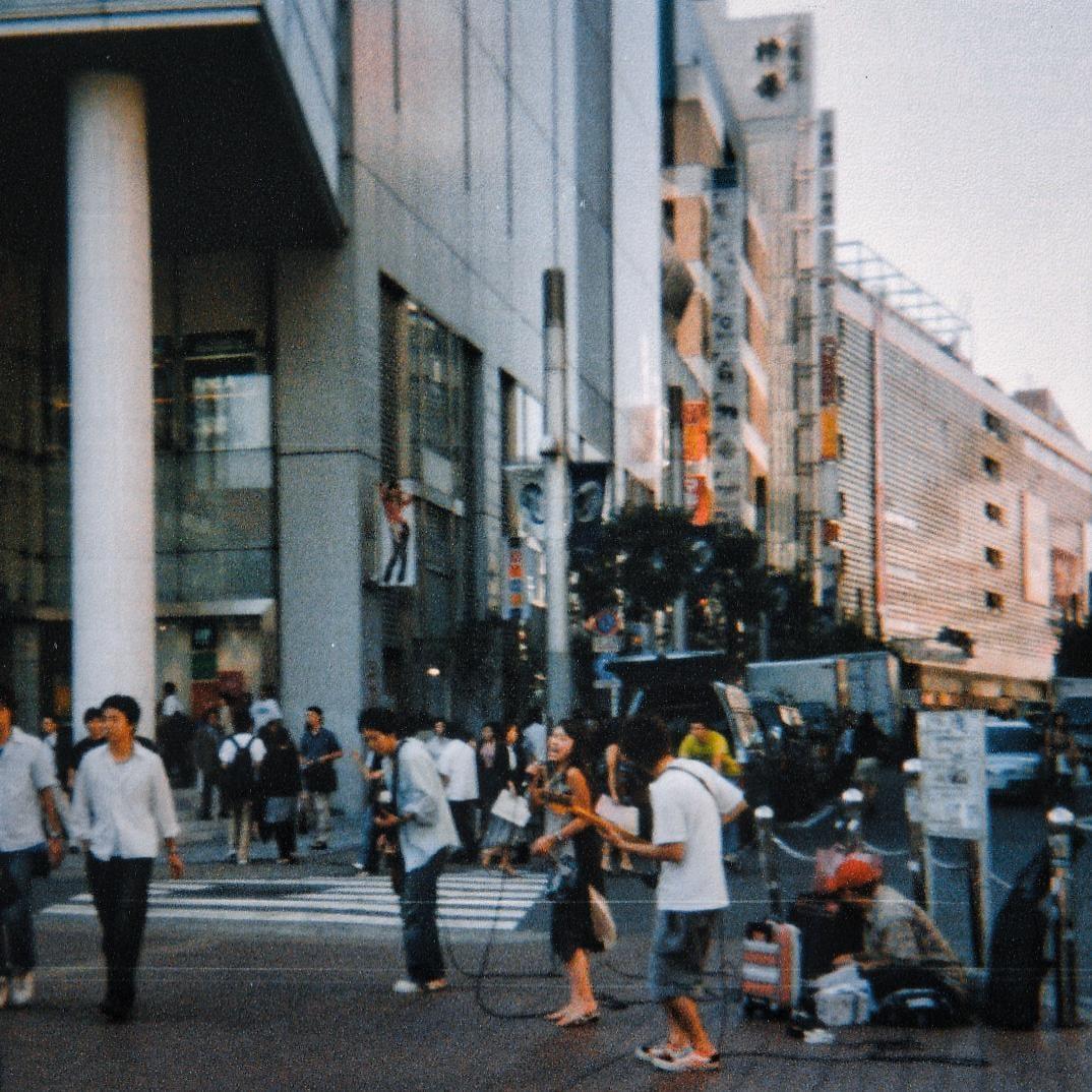 A group of musicians performs on a city street with buildings and pedestrians in the background.