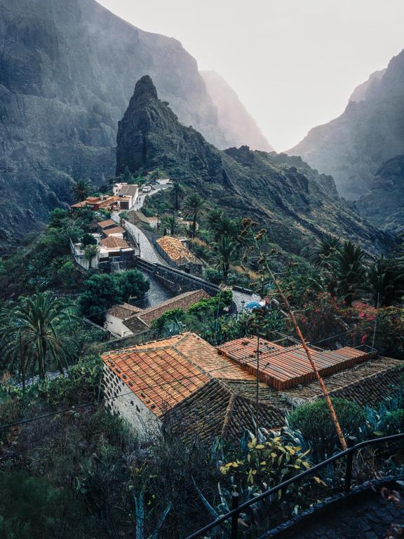 A small village with terracotta roofs is nestled in a valley between steep, rocky mountains.