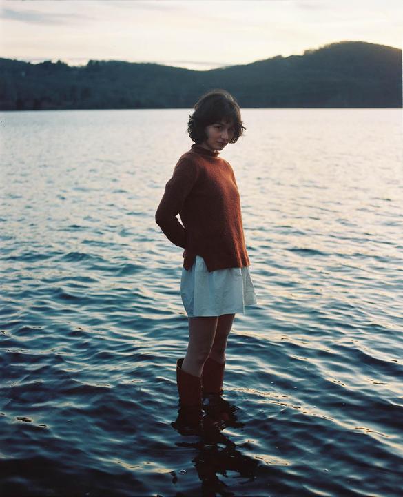 A woman stands in a body of water with mountains in the background.