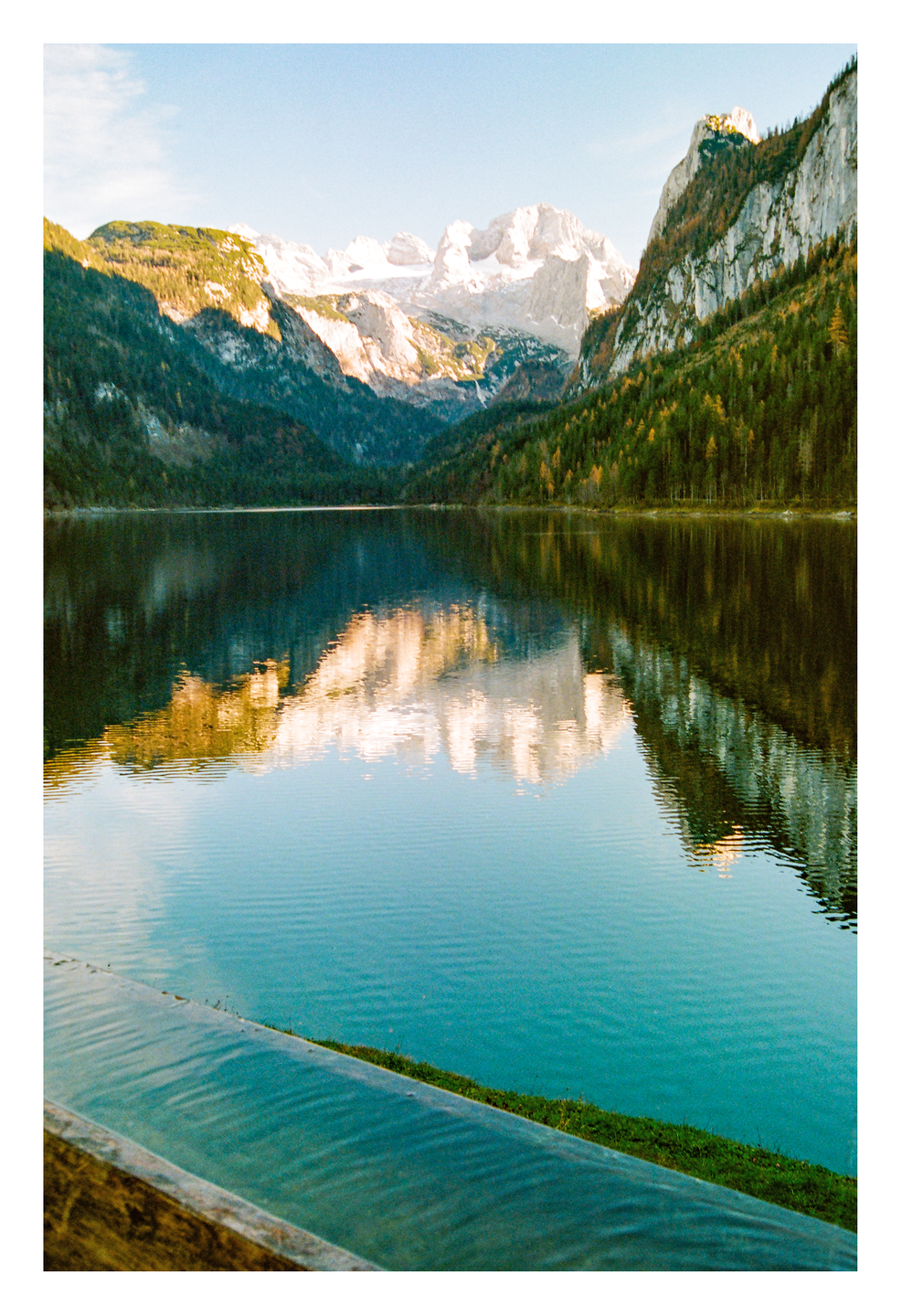 A lake reflects snow-capped mountains and a forest under a clear sky.