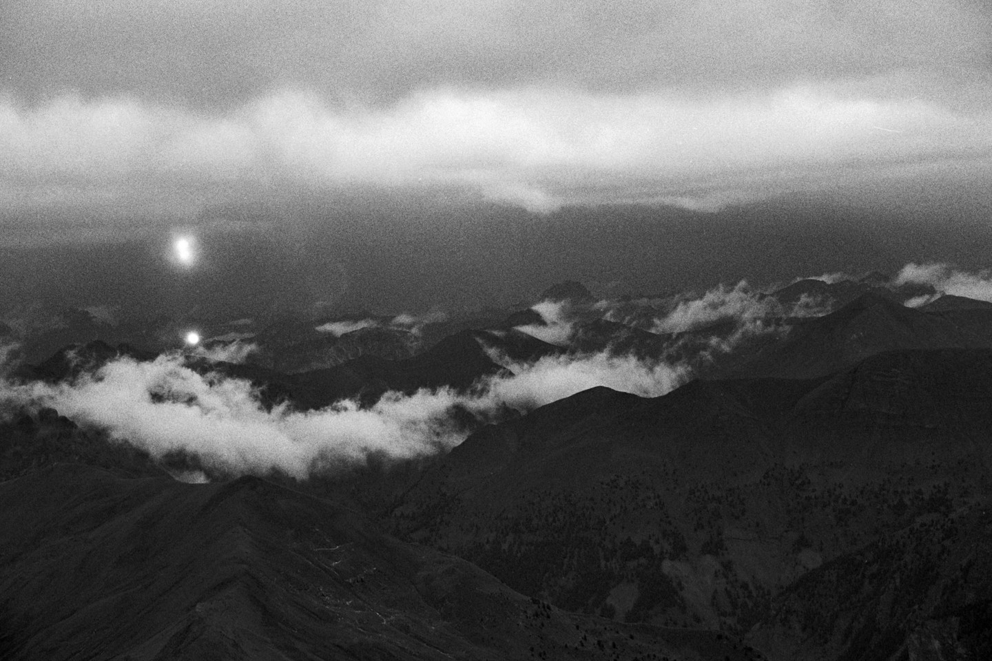 Two bright lights shine above a mountain range covered in clouds.