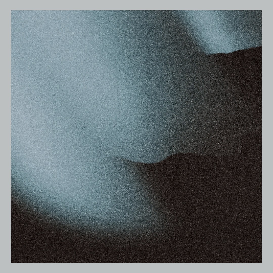 A dark, grainy image shows abstract shapes resembling waves or hills against a lighter, hazy background.