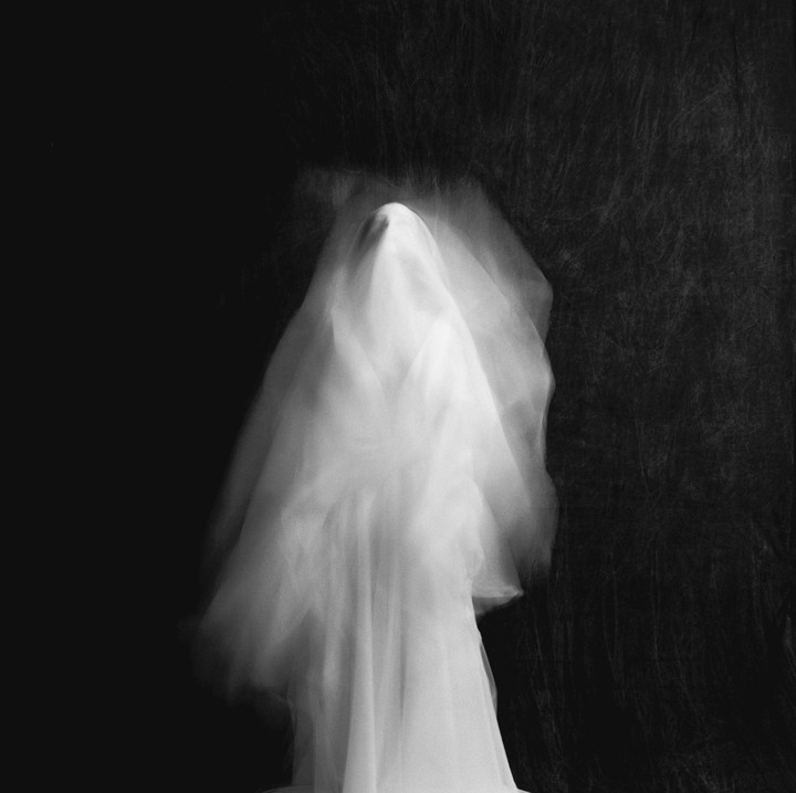 A blurry figure in a white veil stands against a dark background.