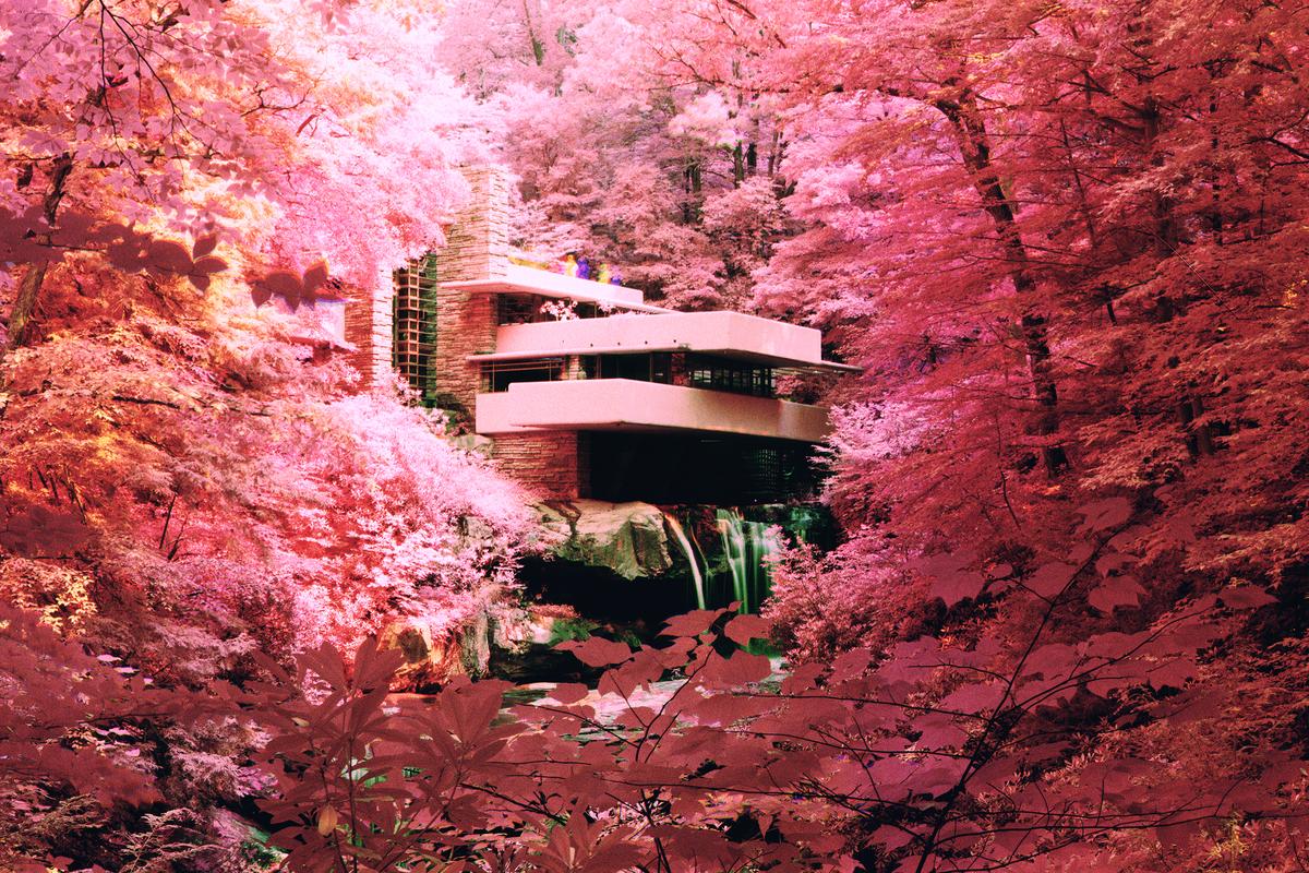 A house with multiple balconies is nestled among vibrant pink trees, with a waterfall visible beneath it.