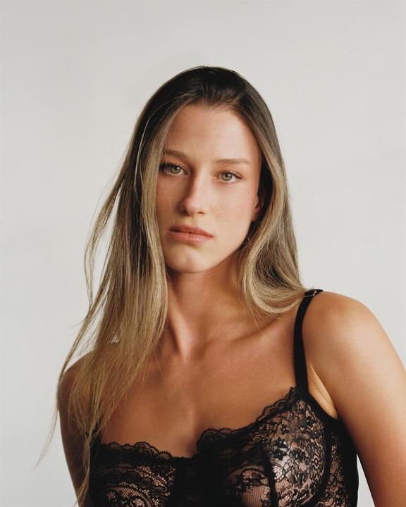 A woman with long hair and a black lace top looks directly at the viewer.
