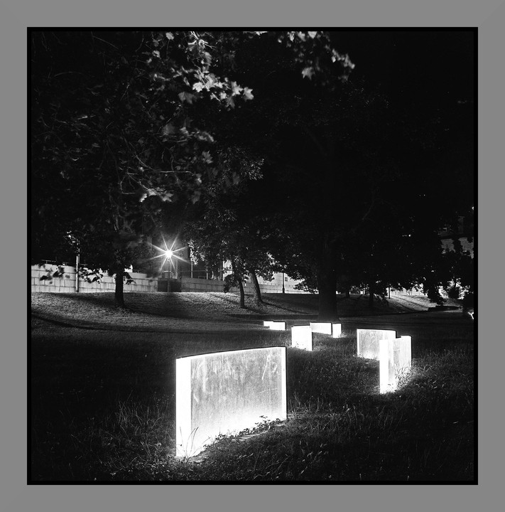 Several glowing rectangular blocks are arranged in a grassy area at night, with trees and a bright street light in the background.