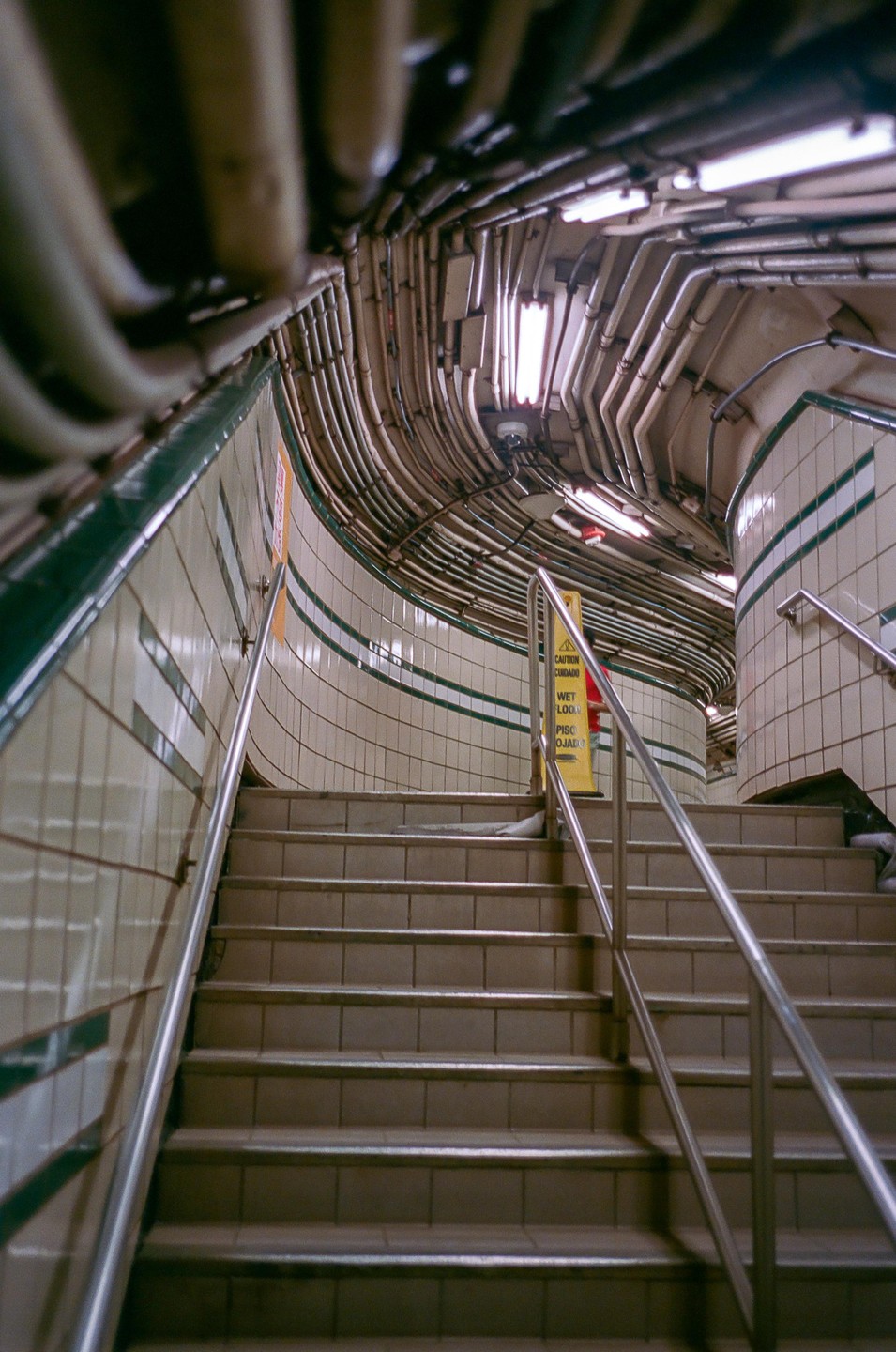 A tiled subway stairwell is visible with many conduits running along the ceiling.