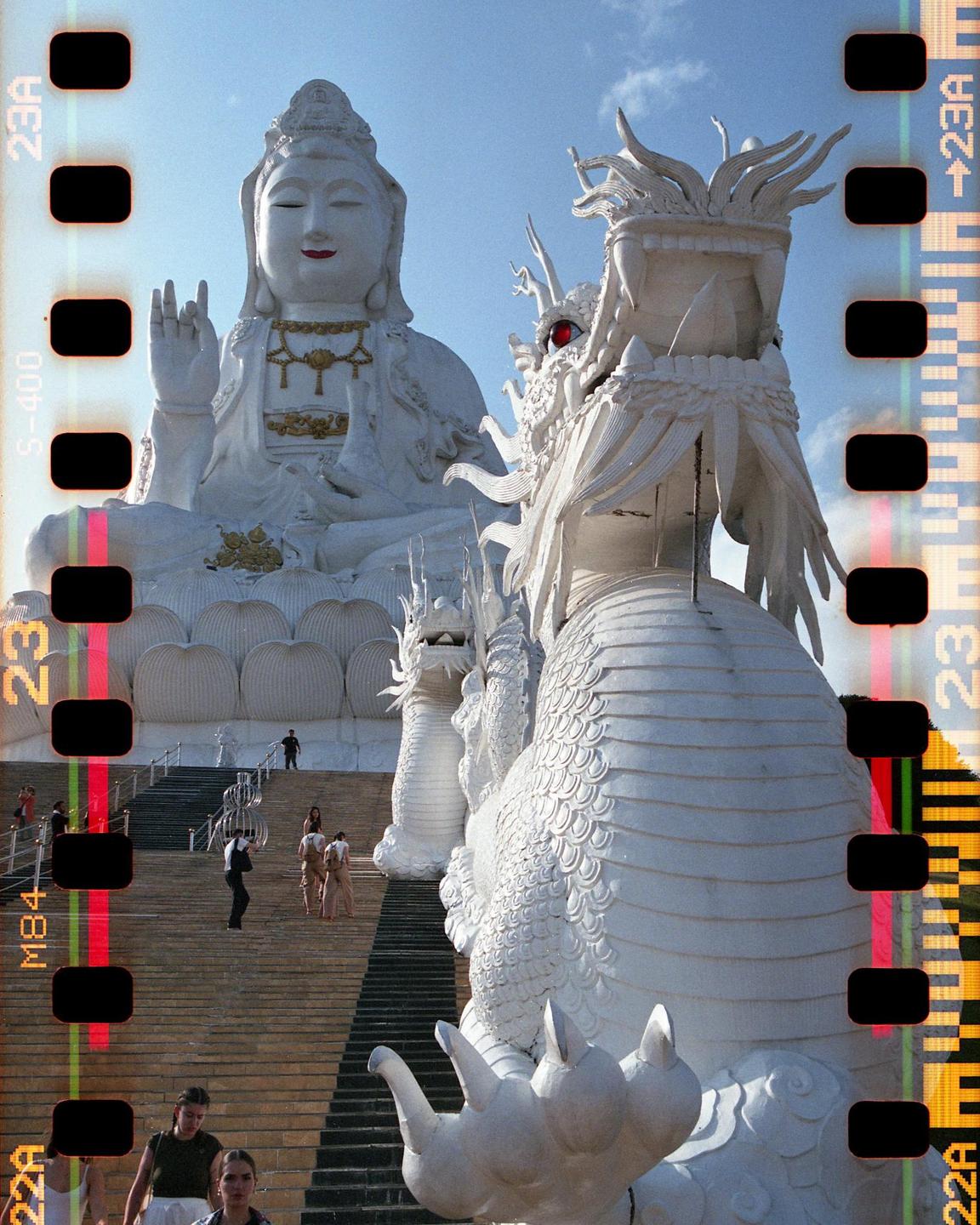 A large white statue of a buddha and a dragon are visible at the top of a long staircase with people walking on it.