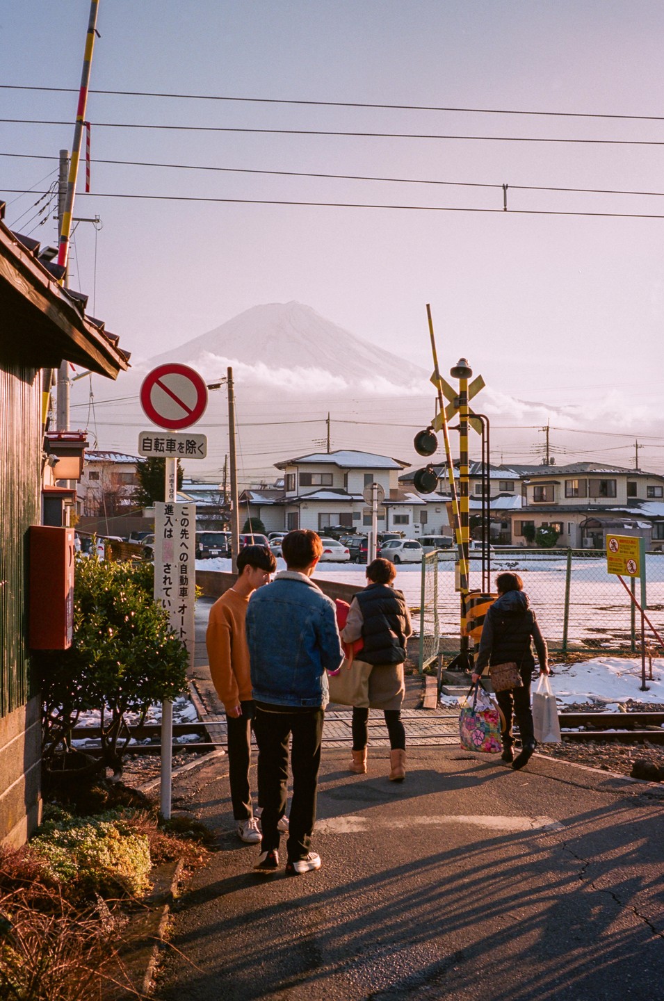 Four people stand at a railroad crossing with Mount Fuji in the background.