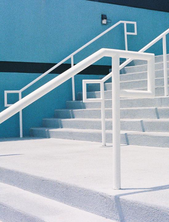 A white railing with geometric shapes leads up a set of stairs next to a blue wall.