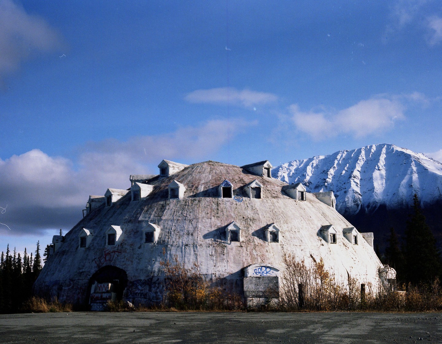 A large, dome-shaped building with many dormer windows sits in front of a snow-capped mountain.