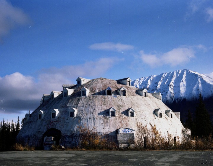 A large, dome-shaped building with many dormer windows sits in front of a snow-capped mountain.