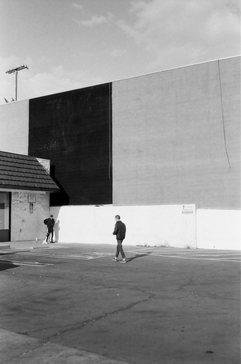 Two men are on a street next to a building with a large black and white wall.