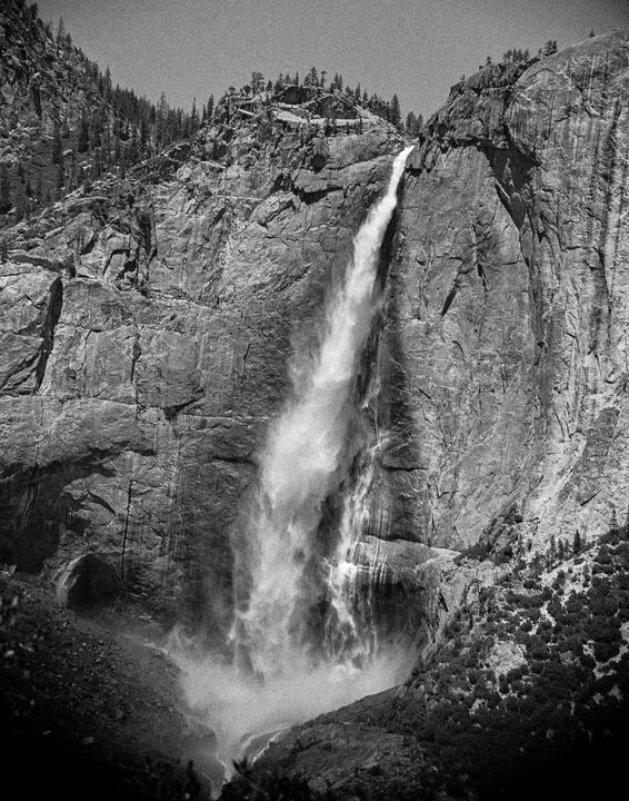 A powerful waterfall cascades down a rocky cliff face, surrounded by trees and mist.