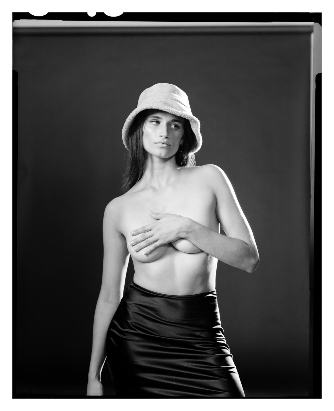 A woman wearing a bucket hat and a long skirt covers her chest with her hand.