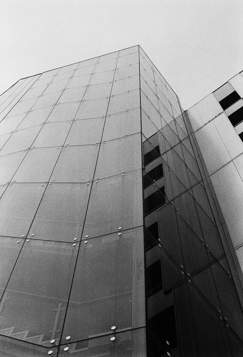 A modern building with a glass facade reflects another building and the sky.