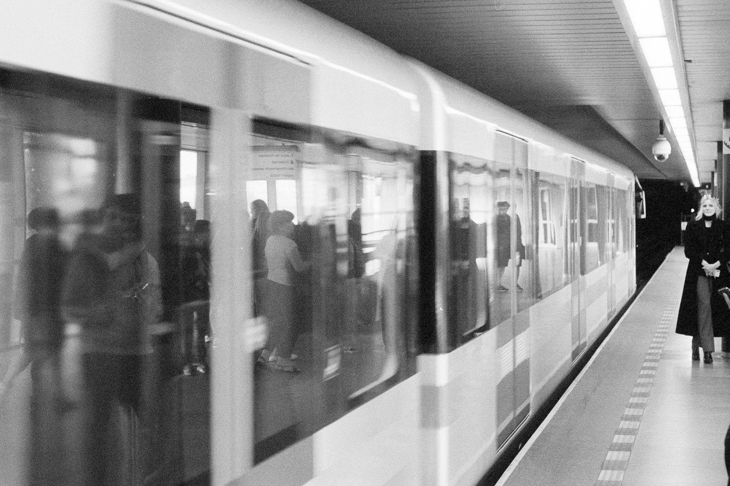 A woman stands on a subway platform as a train passes by, blurring the passengers inside.