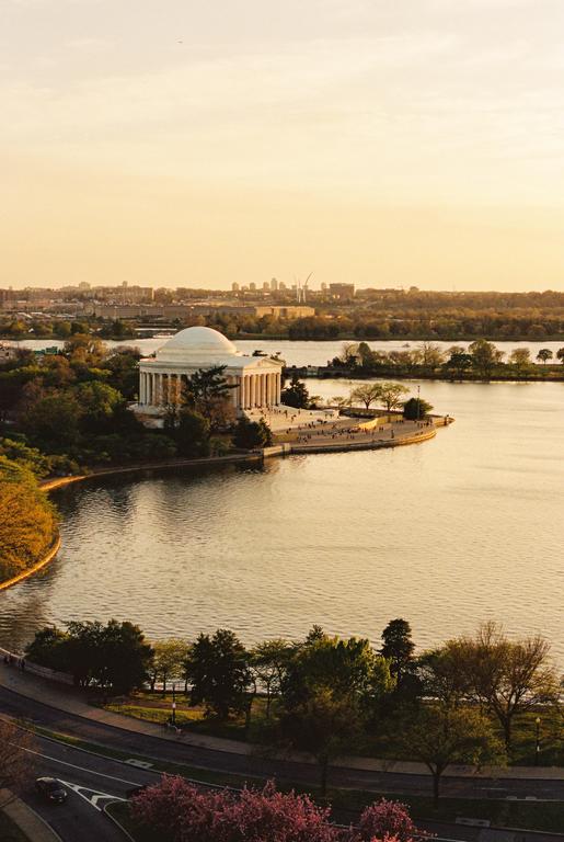 The Jefferson Memorial stands by a body of water with a city skyline in the distance during golden hour.