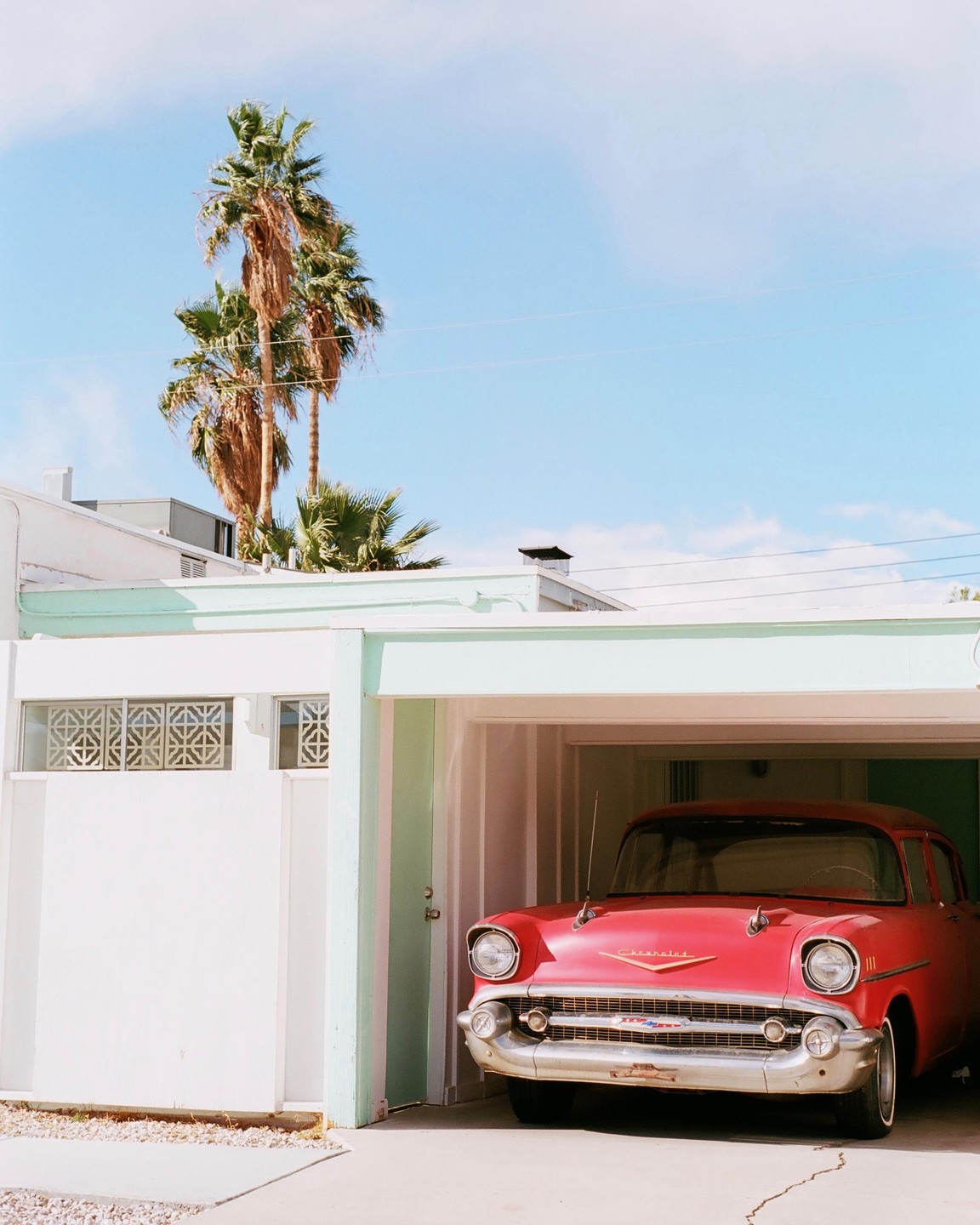 A red vintage car is parked in a garage with palm trees and a blue sky in the background.