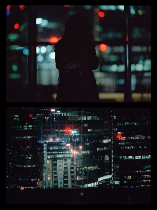 A person stands silhouetted against a window overlooking a city at night, with a second frame showing a close-up of illuminated buildings.