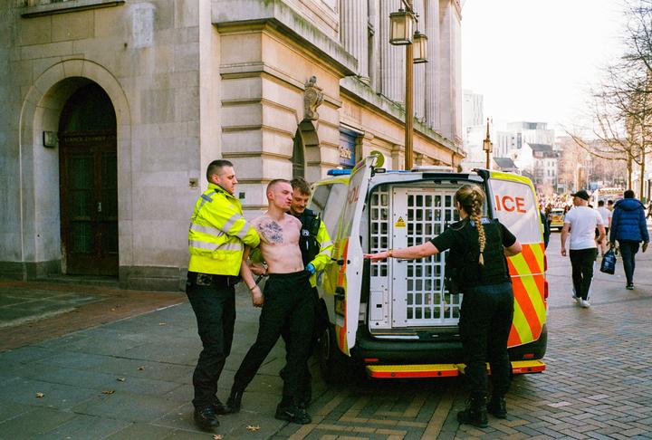 Police officers are arresting a man on a city street next to a police van.