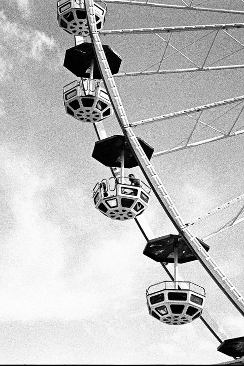 A ferris wheel with several gondolas is captured against a cloudy sky.