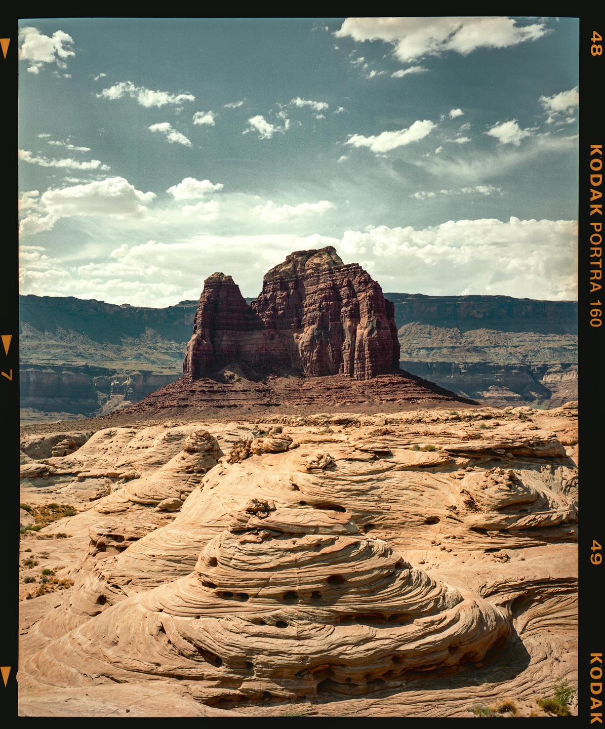 A large rock formation rises from a desert landscape under a cloudy sky.