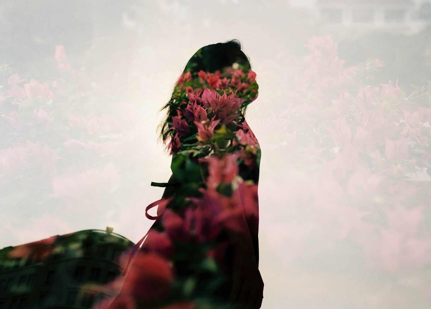 A double exposure shows the silhouette of a woman overlaid with pink flowers and a building.