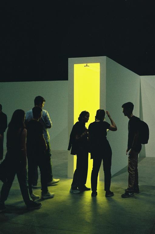 A group of people stand in a dark room illuminated by a bright yellow doorway.