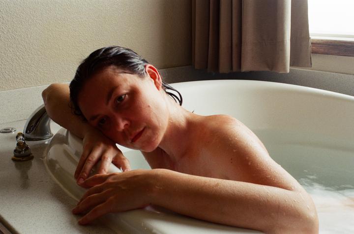 A woman with wet hair rests her head on the edge of a bathtub.