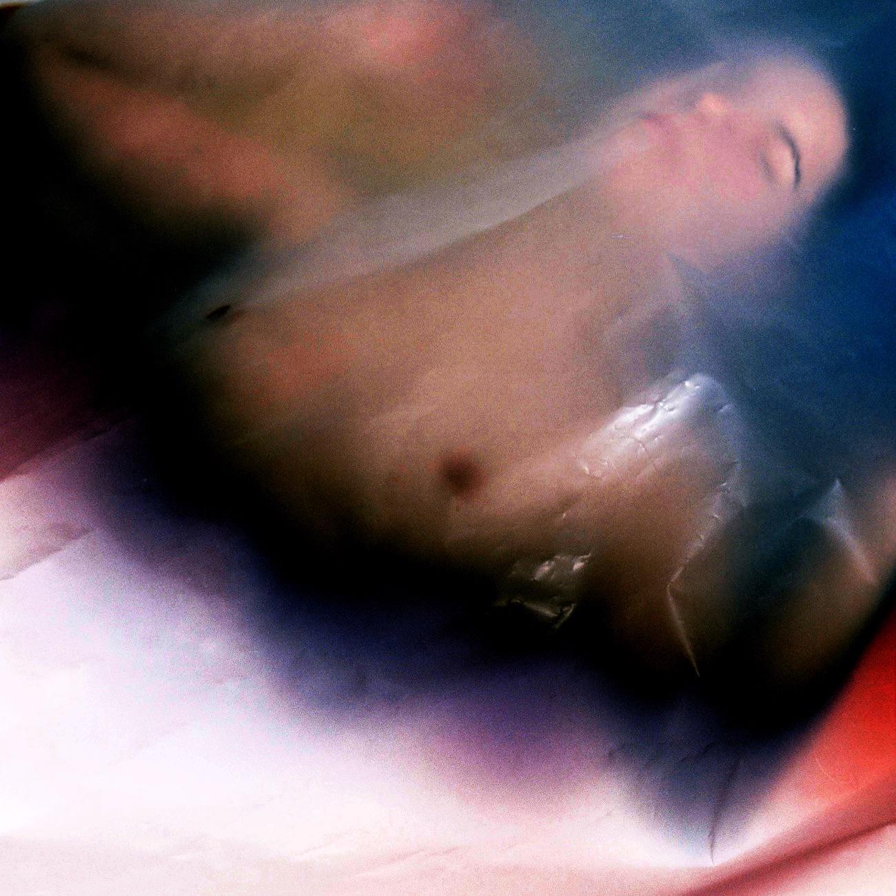A woman's torso and face are visible through a translucent, wrinkled material with color shifts.