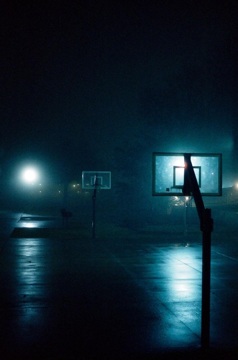 Two basketball hoops stand on a court at night, illuminated by a bright light source.