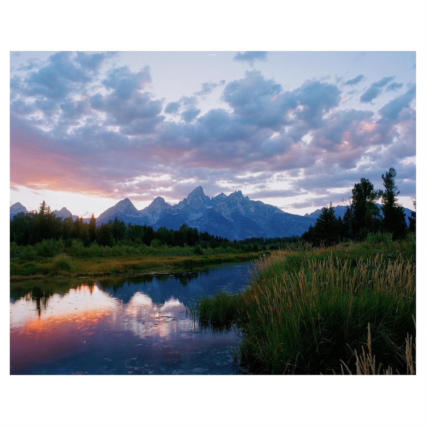 A river reflects the colorful sky and mountains at dusk.