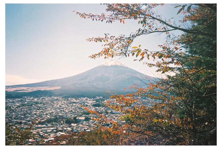 A snow-capped mountain rises above a town, framed by autumn foliage.