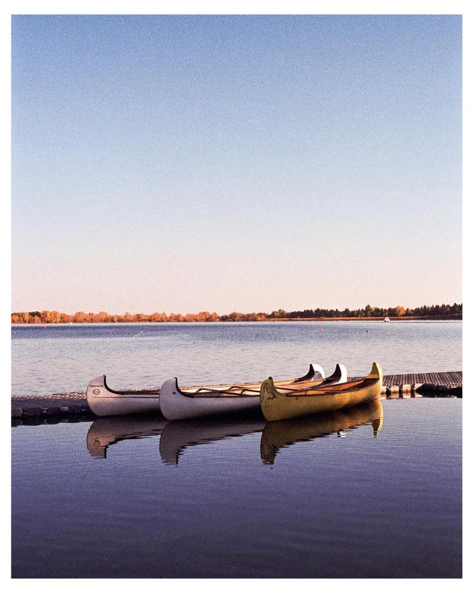 Three canoes are docked on a calm lake with a distant shoreline under a clear sky.