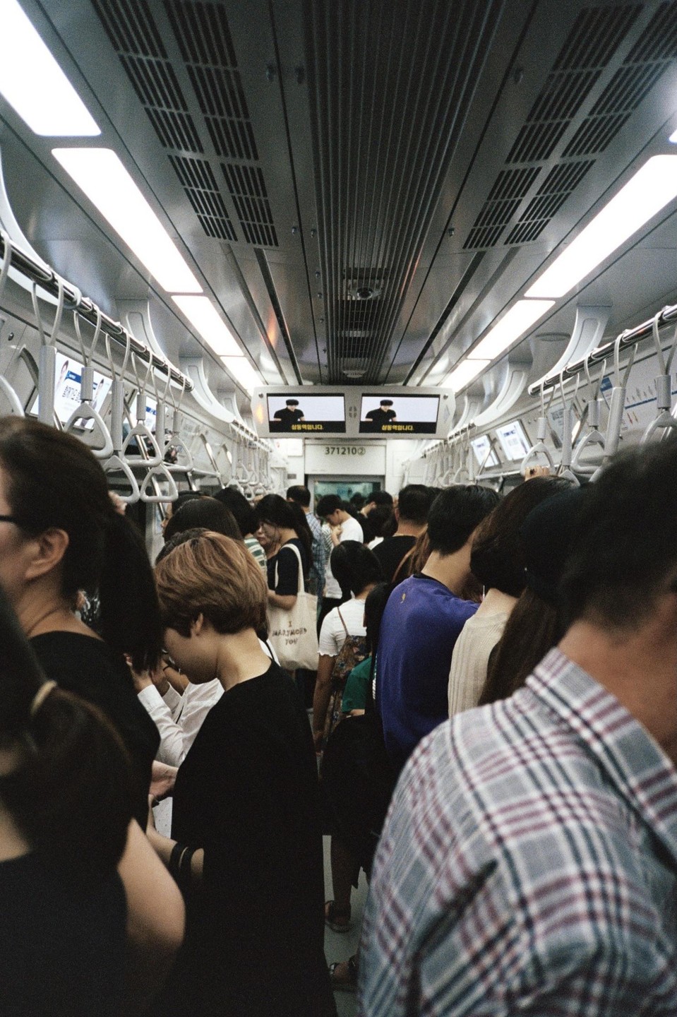 A crowded subway car is filled with people standing and holding onto overhead straps.