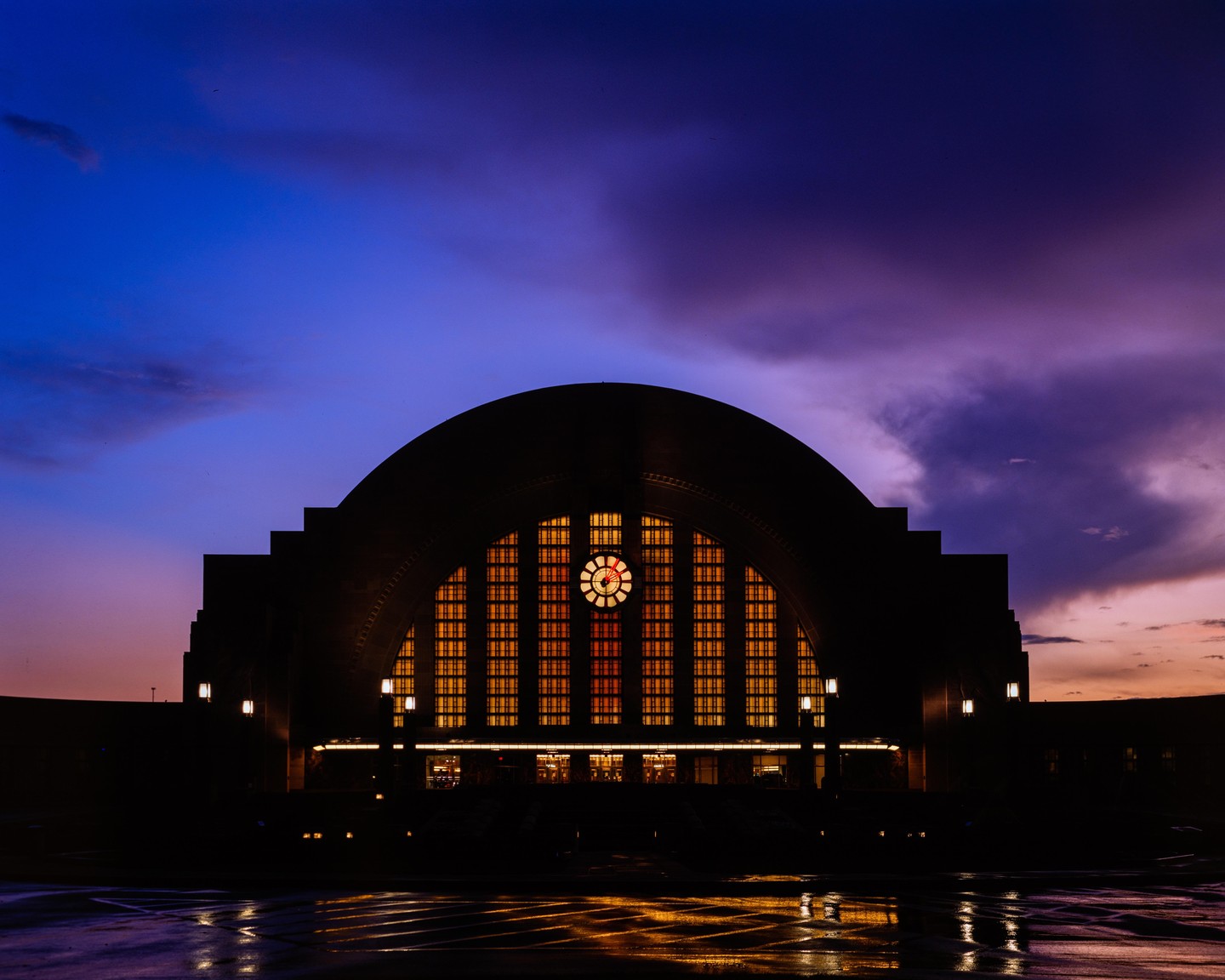 The Cincinnati Union Terminal building is illuminated at dusk, with a dramatic purple and orange sky overhead.