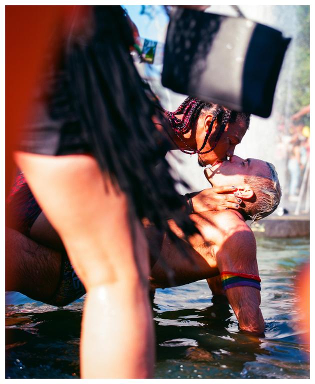 A couple kisses in the water, with one man wearing a rainbow armband.